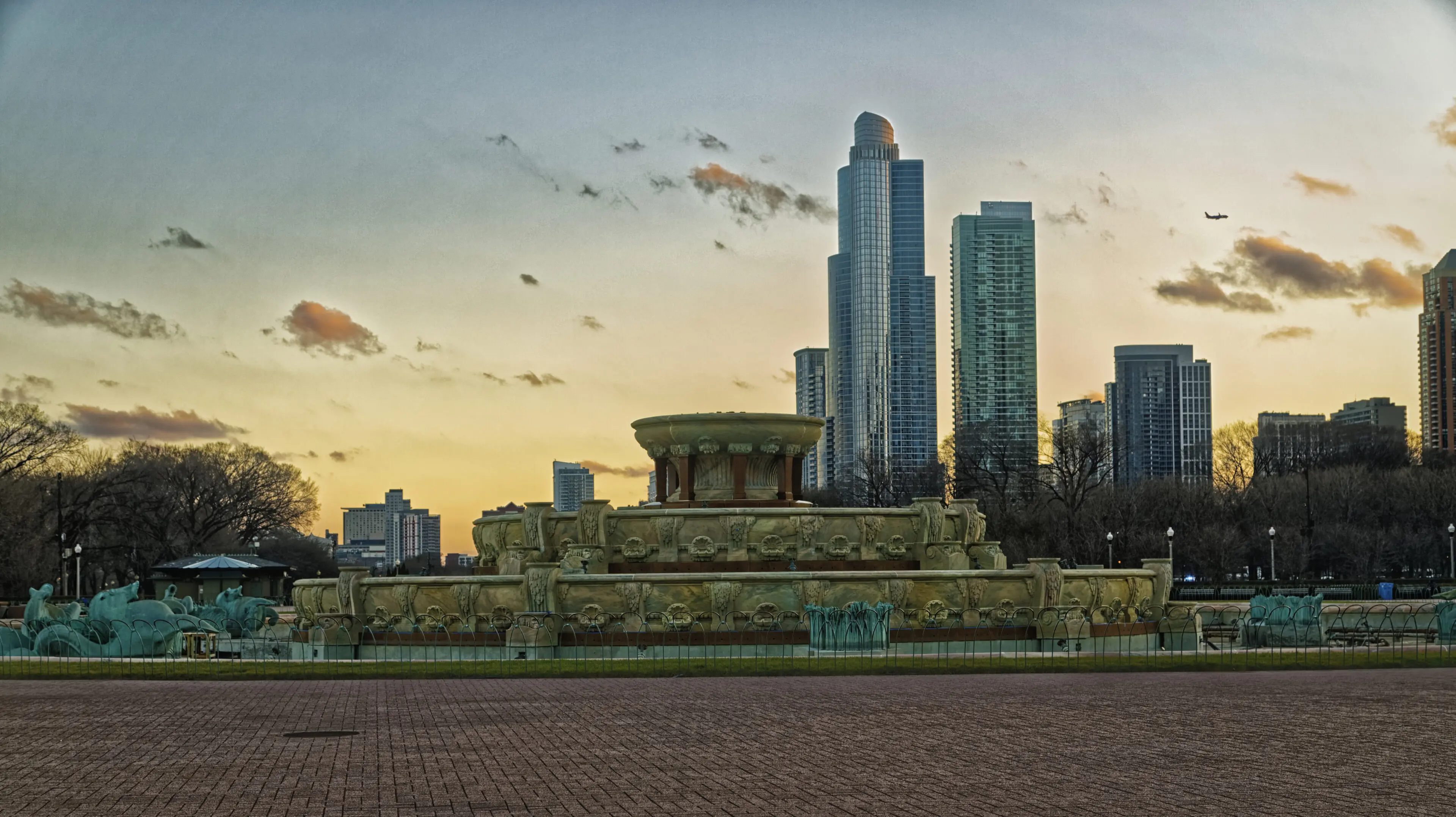 City skyline at sunset with a large ornate fountain in the foreground.